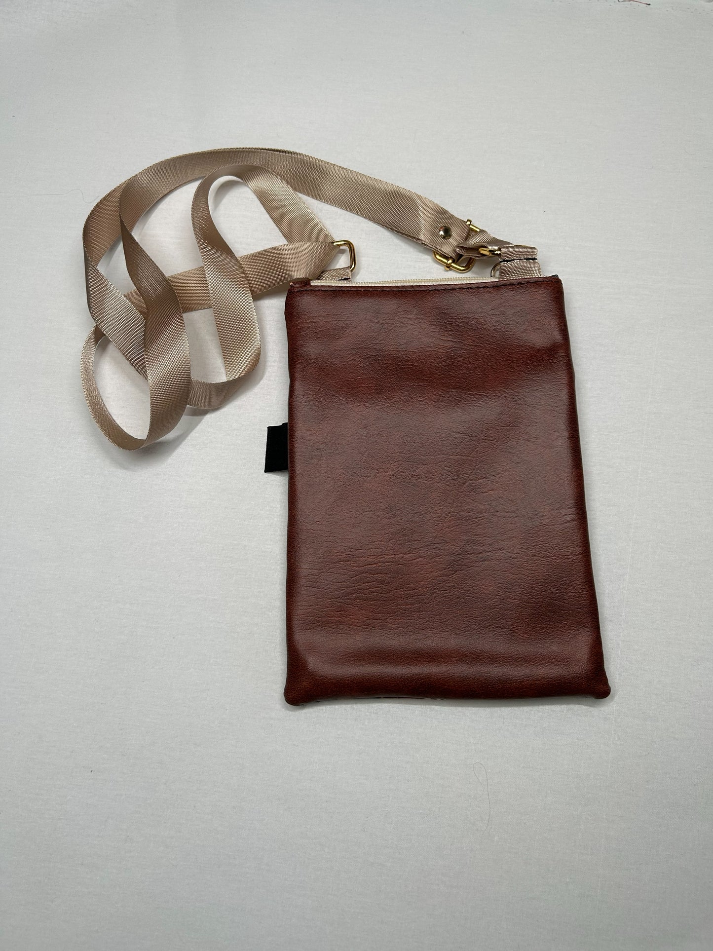 A brown leather crossbody bag with a beige strap is placed on a white surface.