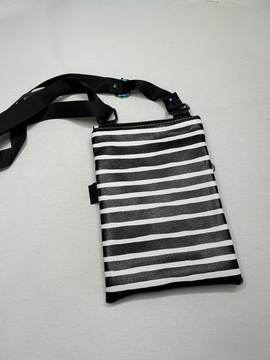 A black and white striped handbag with a black strap and zipper, placed on a white surface.