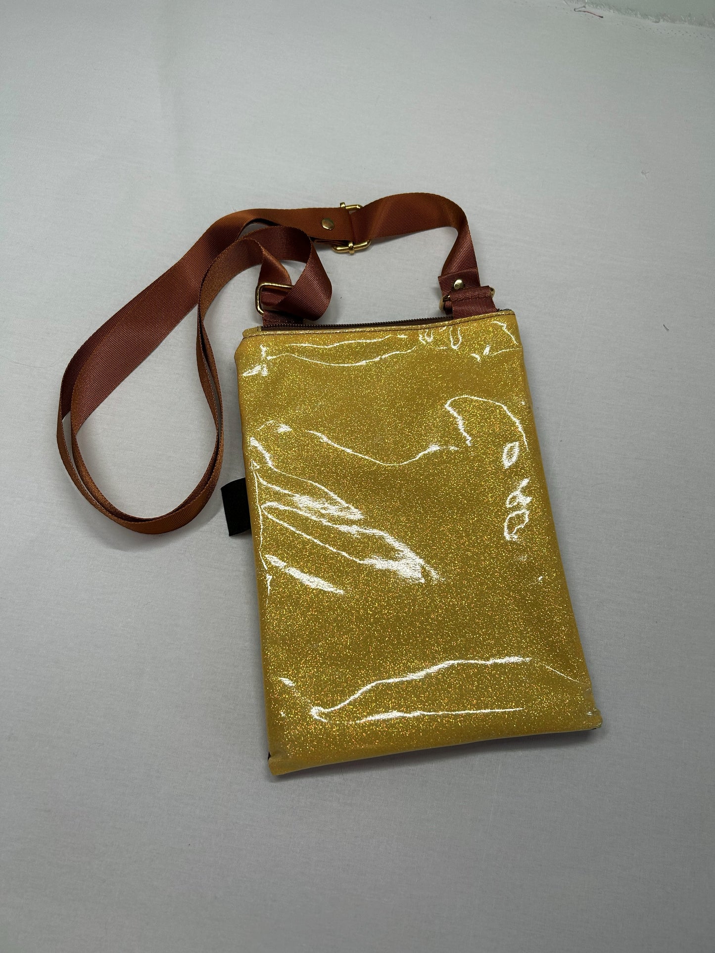 A shiny gold-colored handbag with a brown strap is displayed on a white surface.