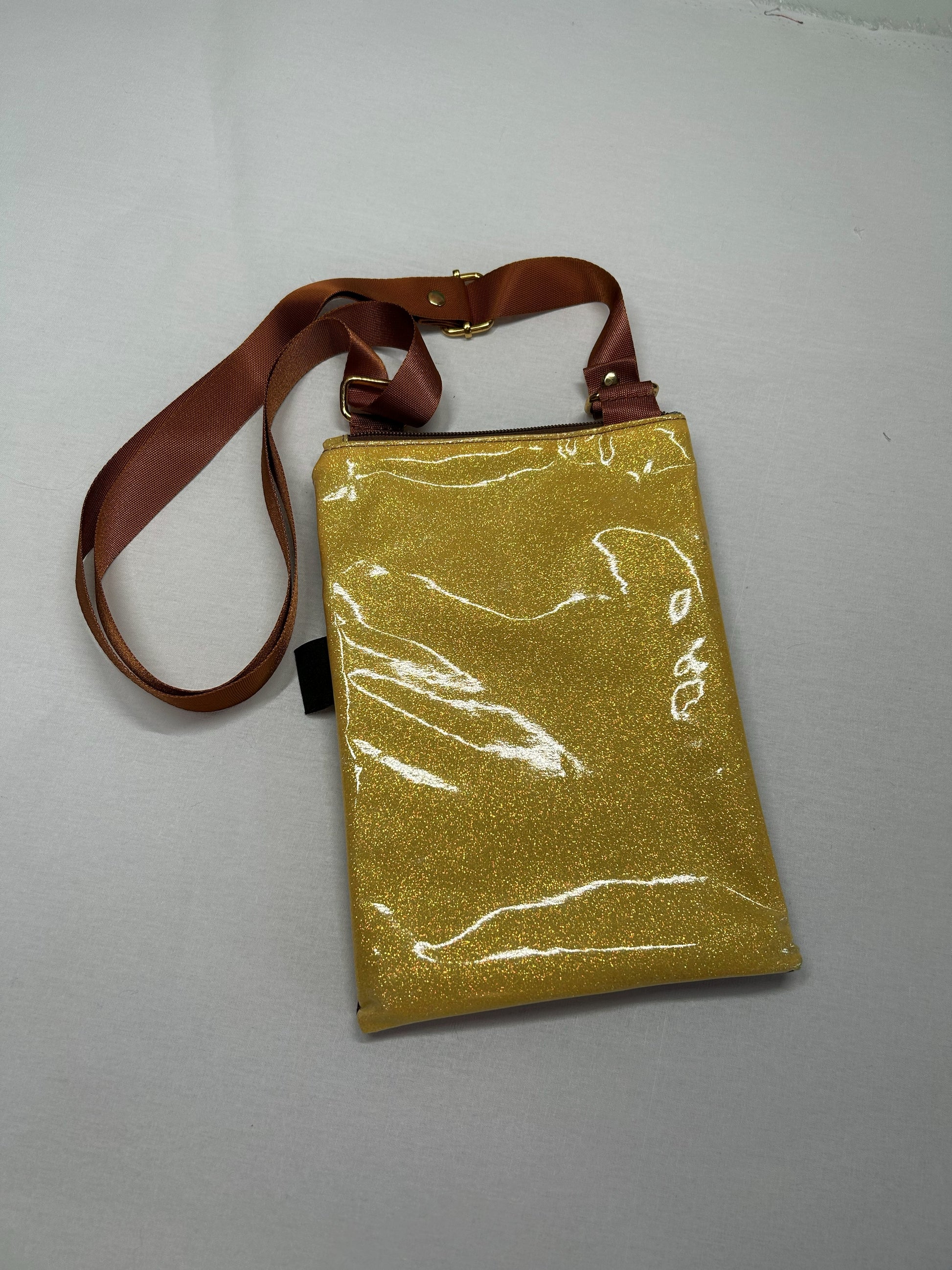 A shiny gold-colored handbag with a brown strap is displayed on a white surface.