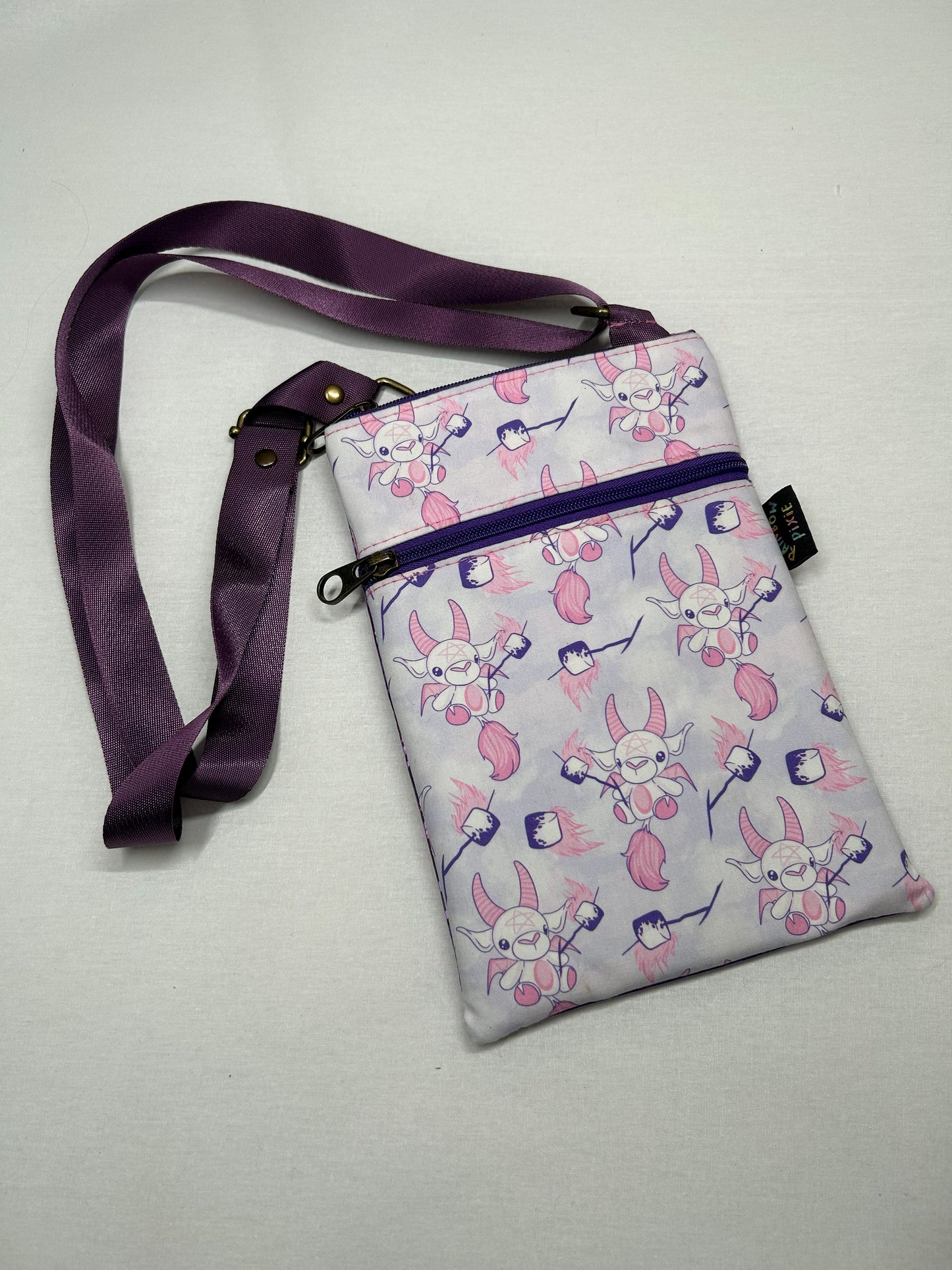 A handbag with a purple strap and a pattern of cartoon-like characters printed on it.