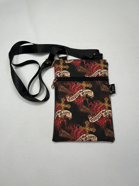 A black crossbody bag with a pattern of red and gold designs, including the text "Vampire Slayer" printed on it.