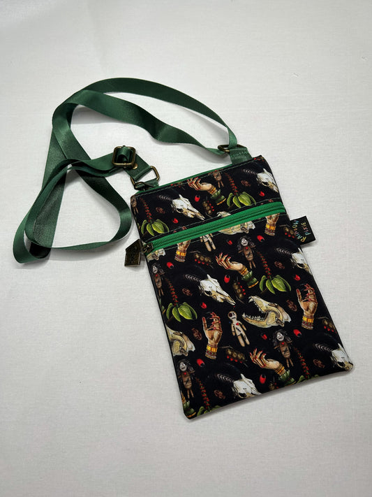 A black purse with a green strap and a pattern of various objects, such as animals, plants, and people, printed on it.