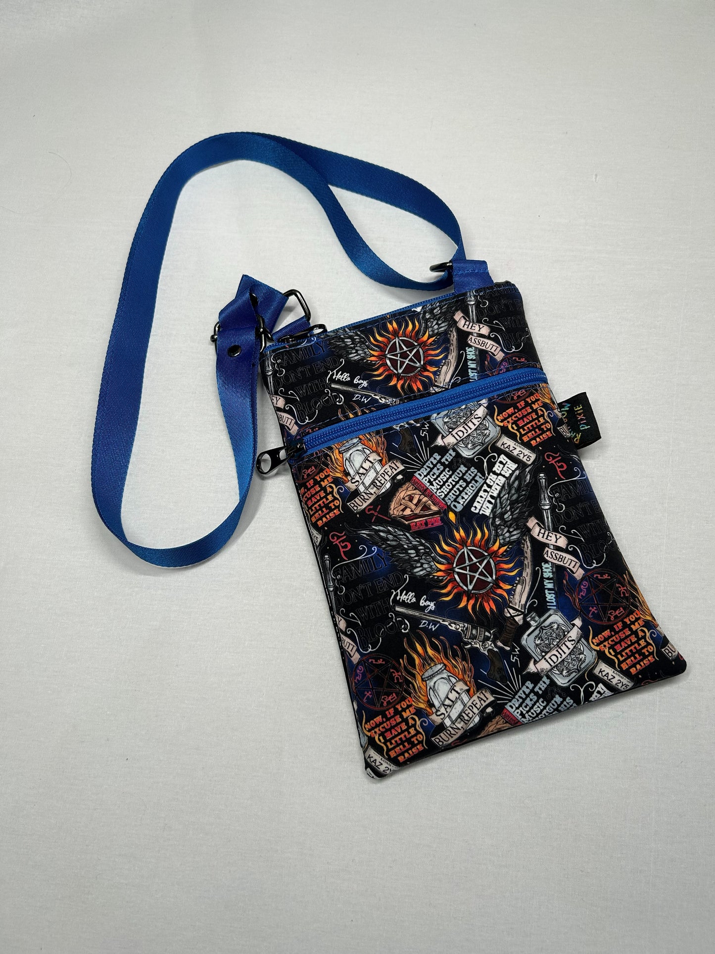 A colorful, patterned crossbody bag with a blue strap and various graphic designs printed on it.
