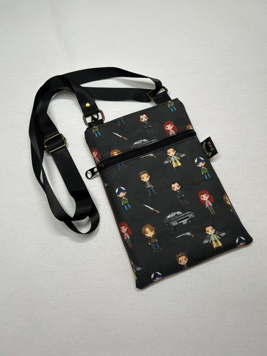 A black crossbody bag with a pattern of cartoon-style characters printed on it.